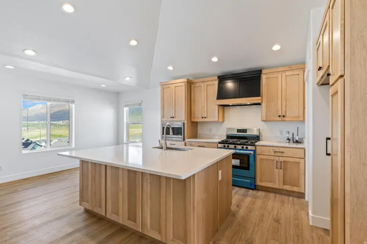 Kitchen featuring a center island with a sink, light wood-finish cabinetry, a gas range, stainless steel appliances, and recessed lighting