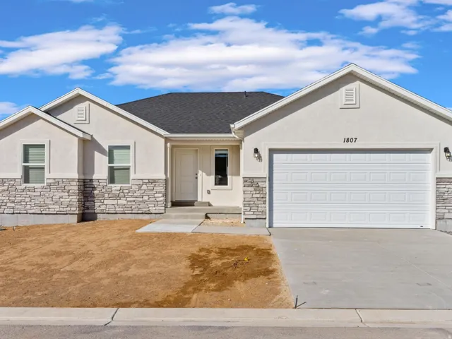 Stucco exterior with stone veneer accents, dark shingle roof, two-car garage, and front entry