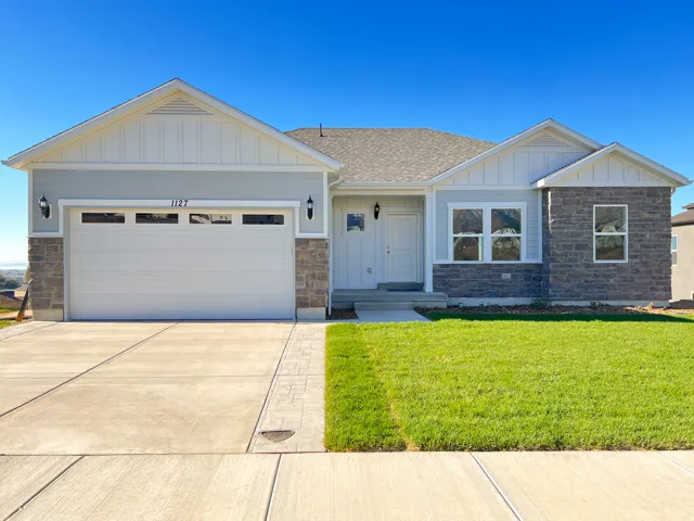 Exterior featuring stone accents, light-toned siding, a two-car garage with a windowed door, a concrete driveway, and a manicured lawn