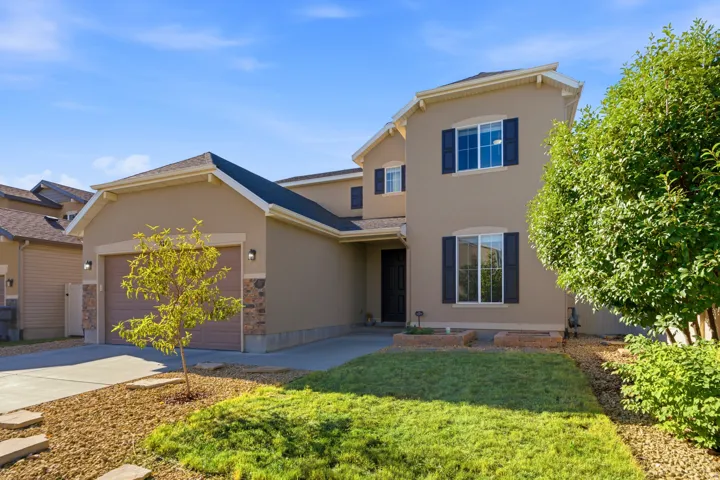Two-story stucco exterior with decorative shutters, integrated two-car garage, concrete driveway, and stone accents
