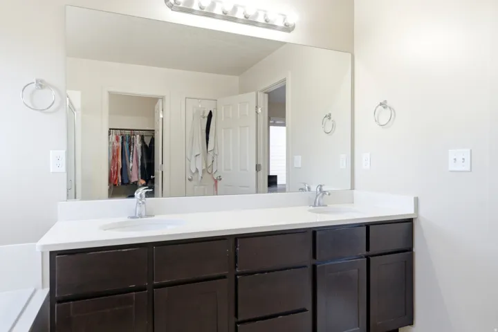 Dual basin vanity with dark wood-finish cabinetry, white countertop, and chrome fixtures