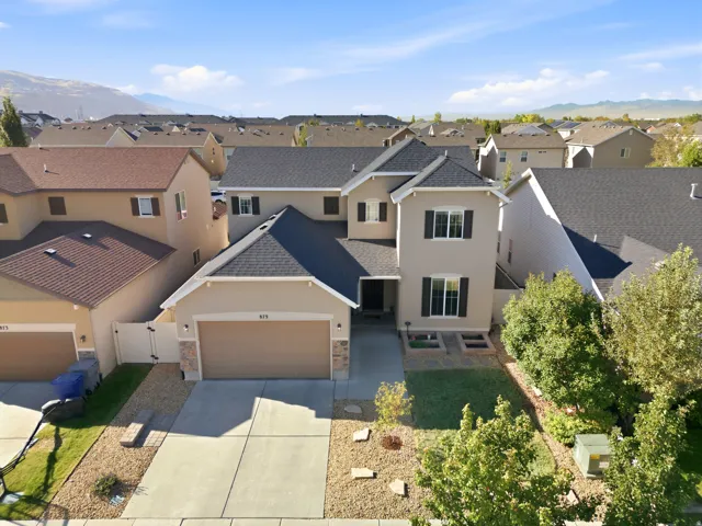 Stucco exterior with stone accents, dark shingle roof, two-car garage, and established front yard landscaping