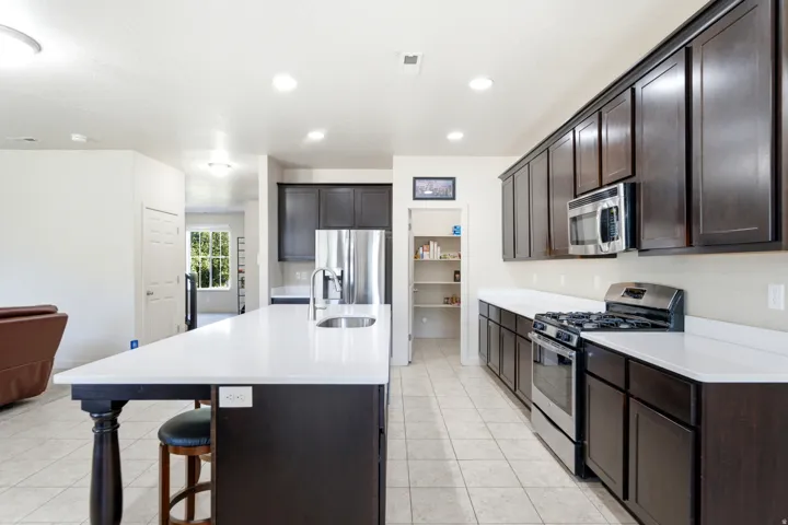 Kitchen featuring a large island with a white countertop, dark wood-finish cabinetry, stainless steel appliances, and tiled flooring