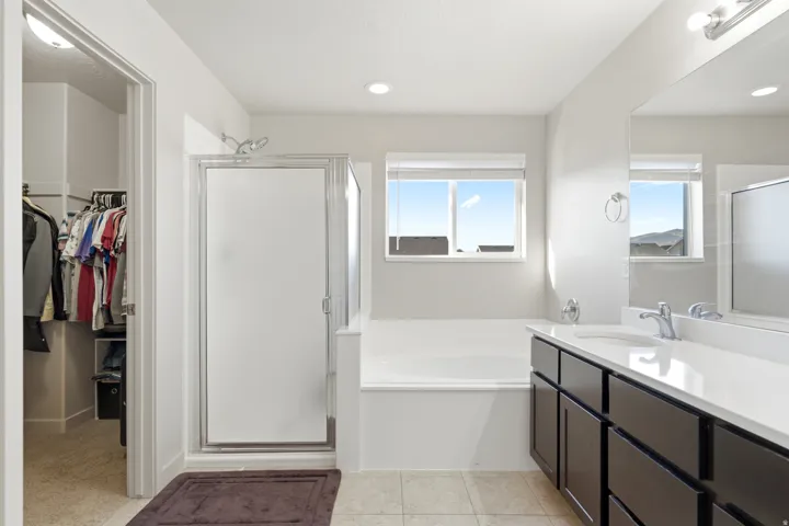 Bathroom featuring a built-in soaking tub, glass-enclosed shower, dual vanity with white countertops, and tiled flooring