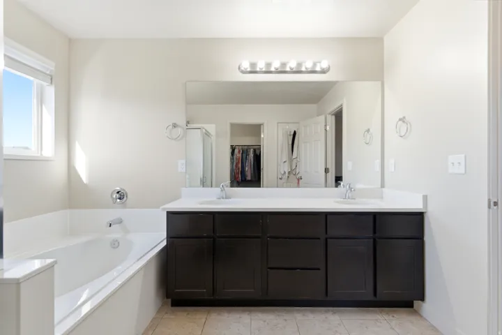 Built-in soaking tub, large vanity with dual sinks, spacious counter, and overhead lighting