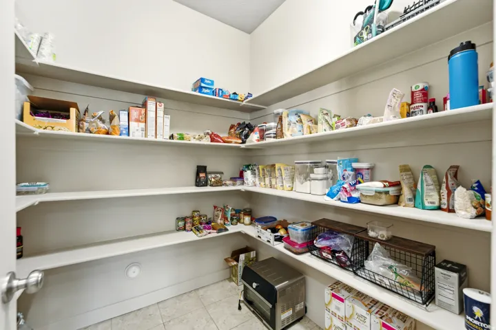 Walk-in pantry with extensive built-in shelving, white walls, and tiled flooring