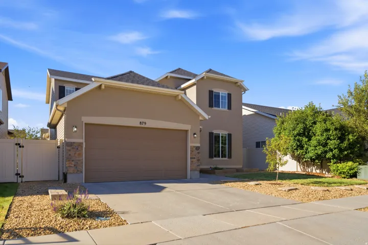 Stucco exterior with stone accenting, attached two-car garage, paved driveway, and established landscaping