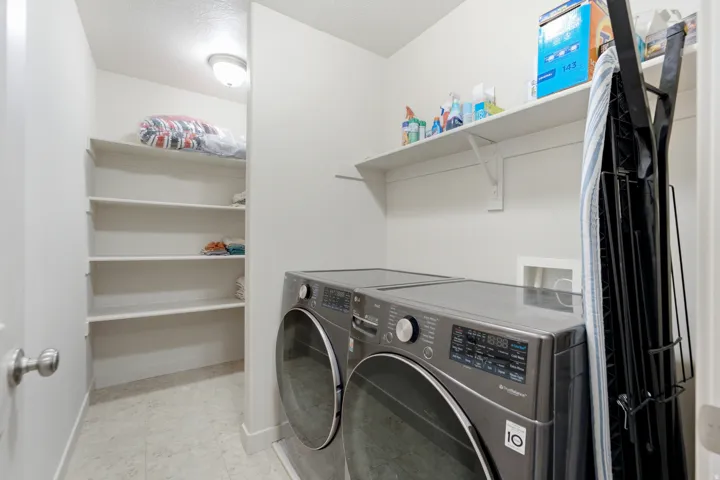 Laundry area with white walls, overhead lighting, an integrated shelving unit, and a tiled floor
