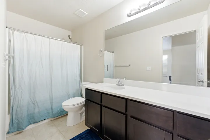 Bathroom featuring a dark wood-finish vanity with a white countertop, an integrated sink, a large wall-mounted mirror, and a shower-over-tub combination