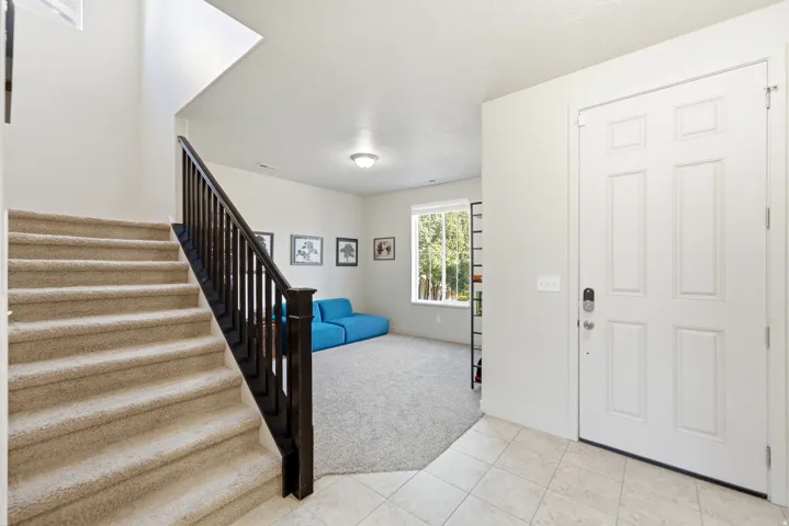 Entryway featuring a paneled door, tiled flooring, and a carpeted staircase with a dark wood-finish railing