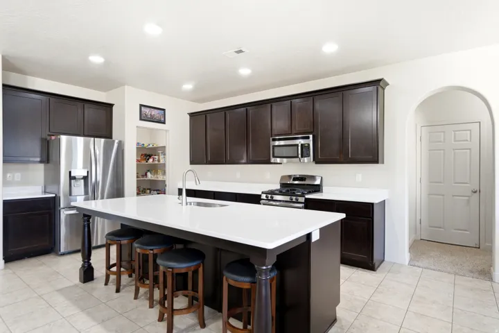 Kitchen featuring dark wood-finish cabinetry, white countertops, a stainless steel refrigerator, and a kitchen island with seating