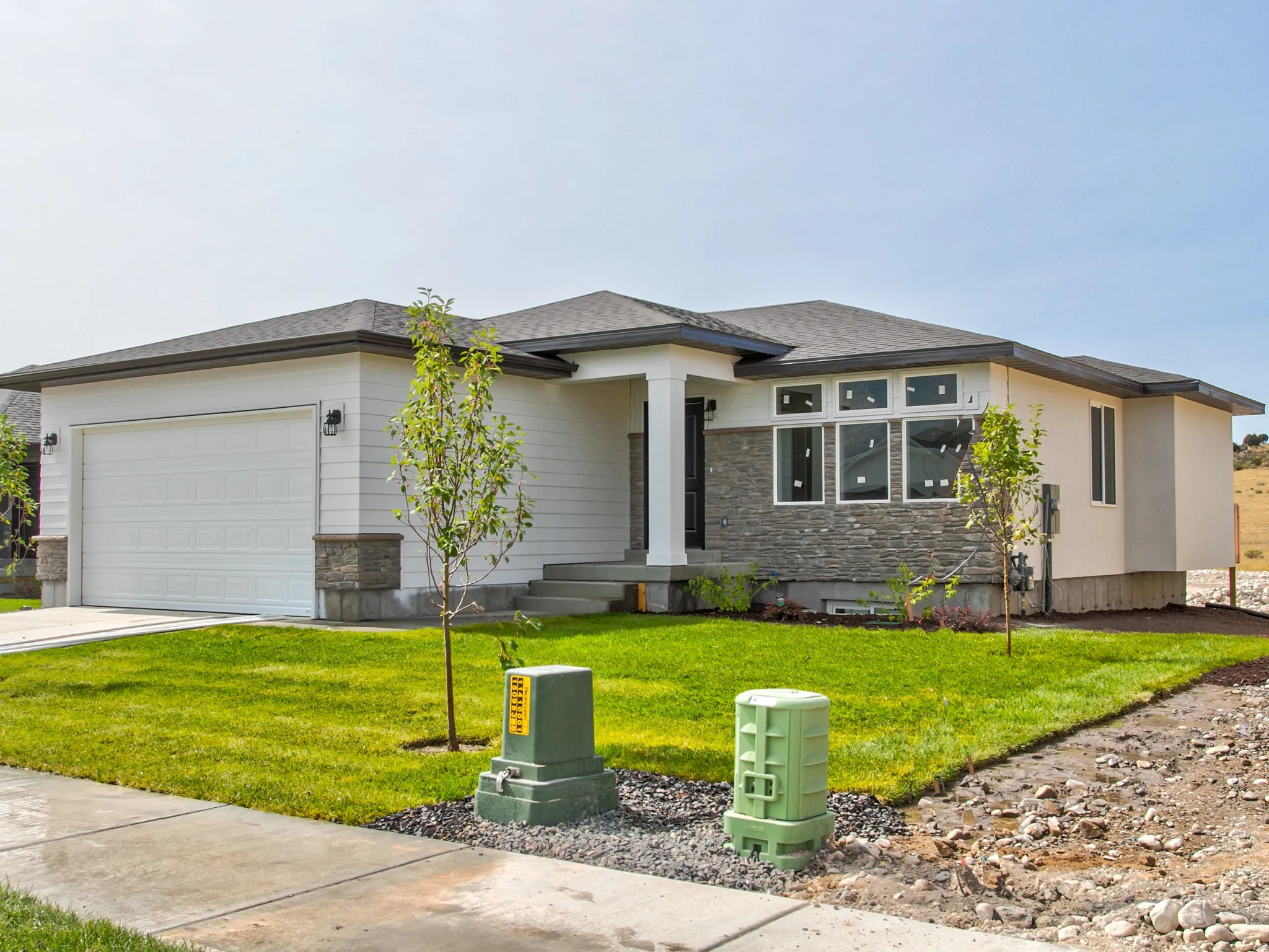 Single-story residence featuring a white siding exterior, stone accents, a two-car garage, and a manicured front lawn