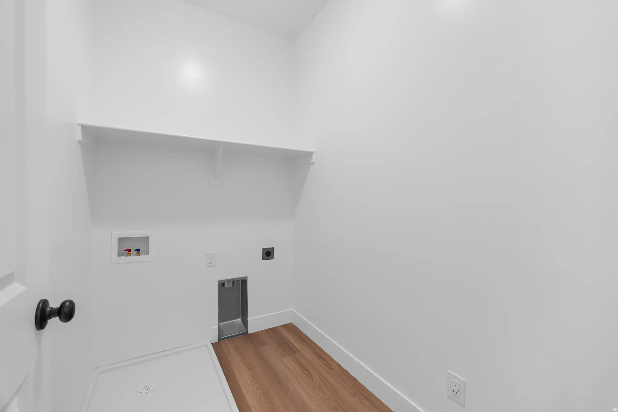 Dedicated laundry area featuring a built-in shelf, wood-finish flooring, and white walls