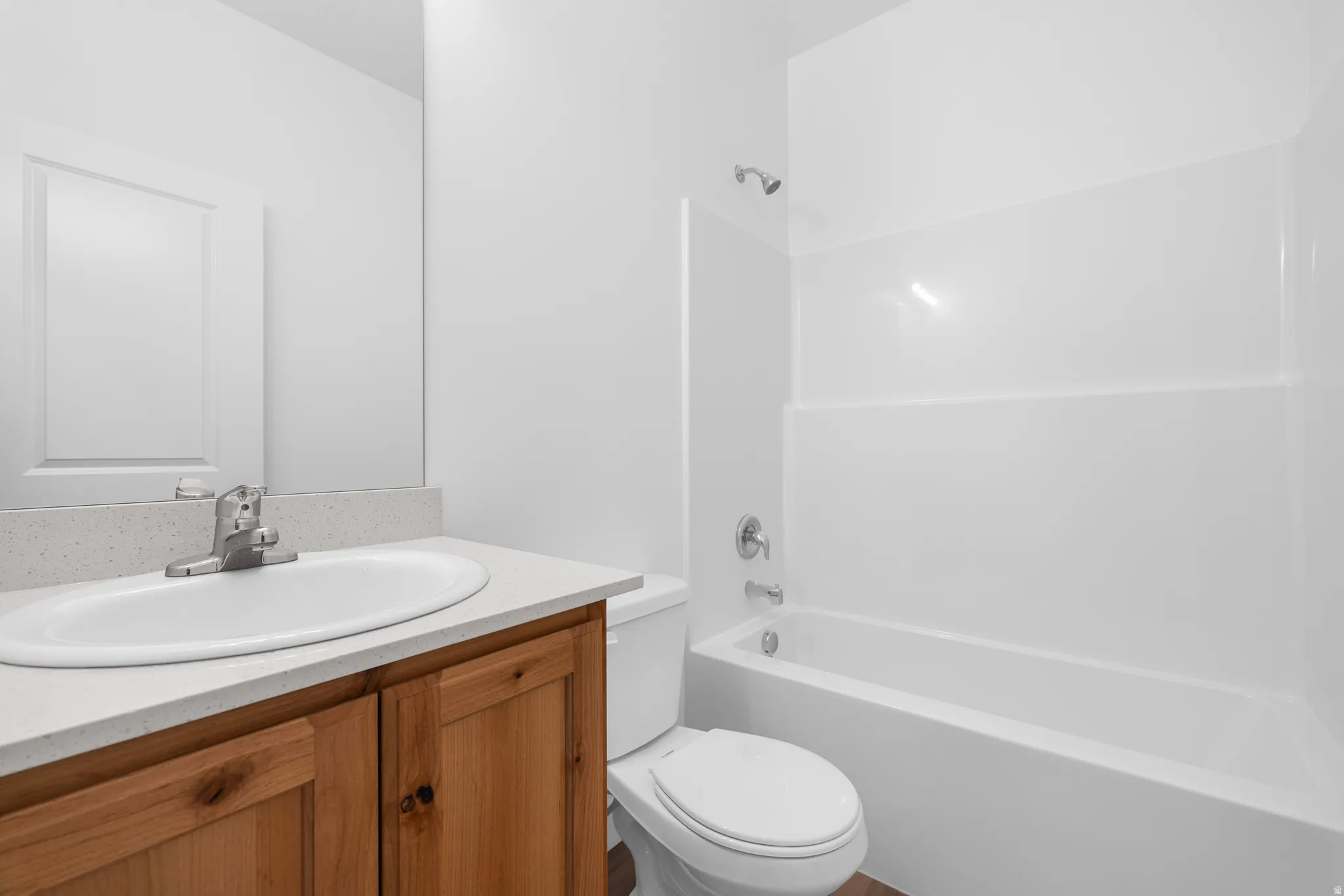 Bathroom featuring a wood-finish vanity, light-toned countertop, oval undermount sink, and a white shower-tub combination