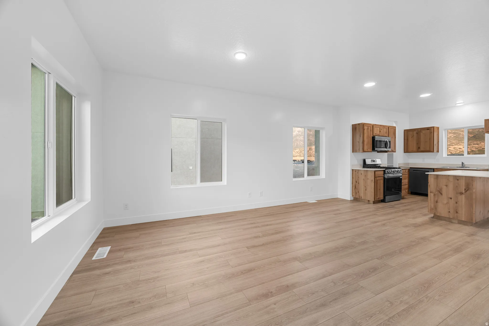 Wood-finish flooring, recessed lighting, white walls, wood-finish cabinetry, and a kitchen island with a light-toned countertop