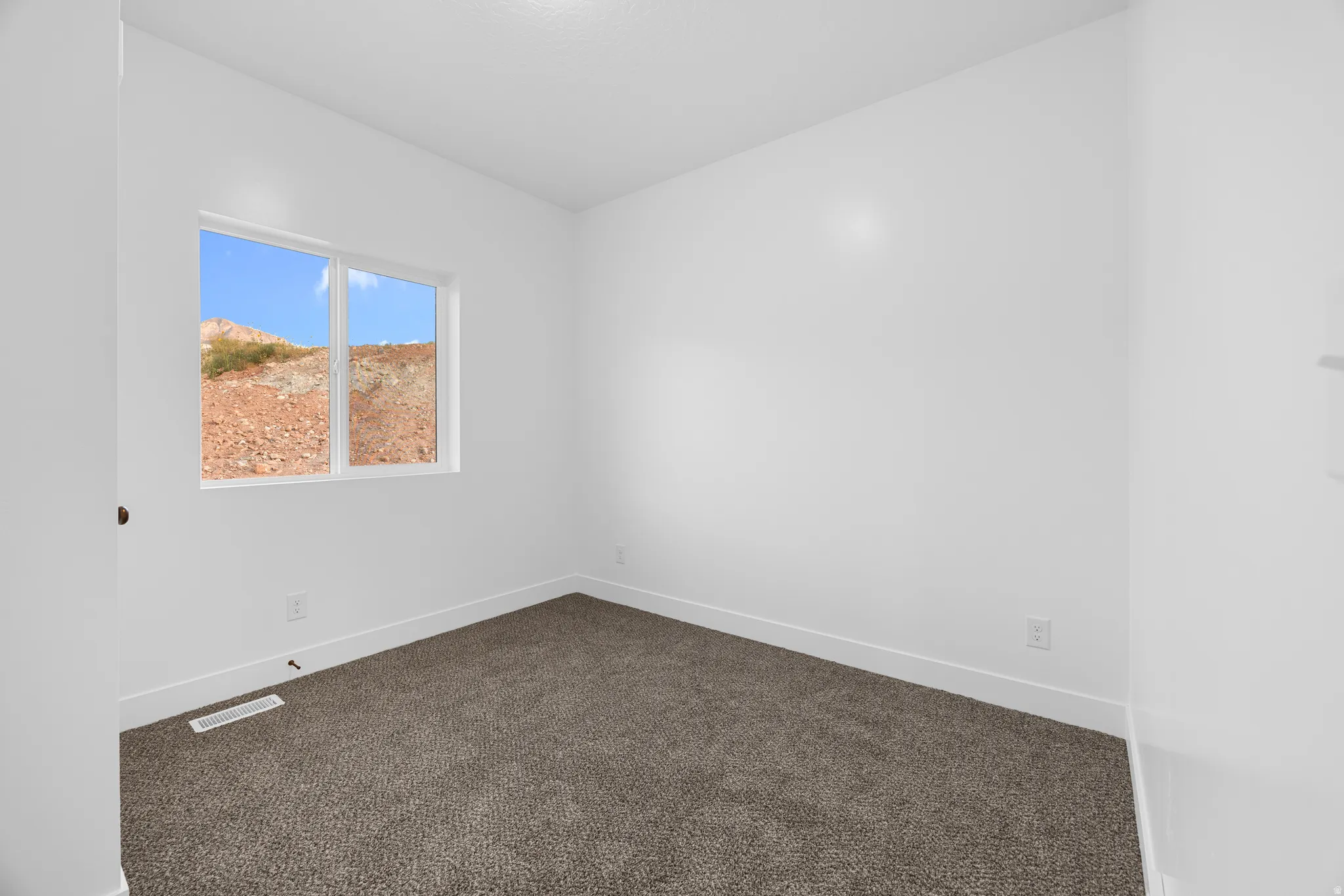 Window with exterior scenery, neutral tone carpeting, and crisp white walls