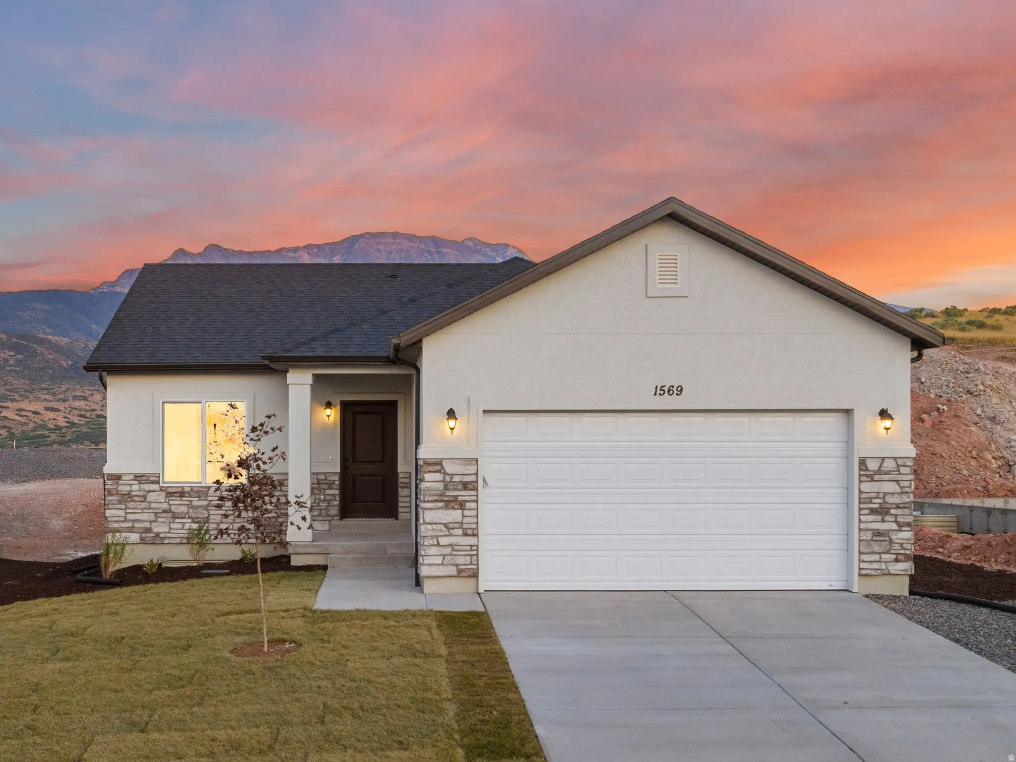 Contemporary home with a dark shingle roof, stone and stucco exterior, an attached garage, a concrete driveway, and a partially landscaped yard