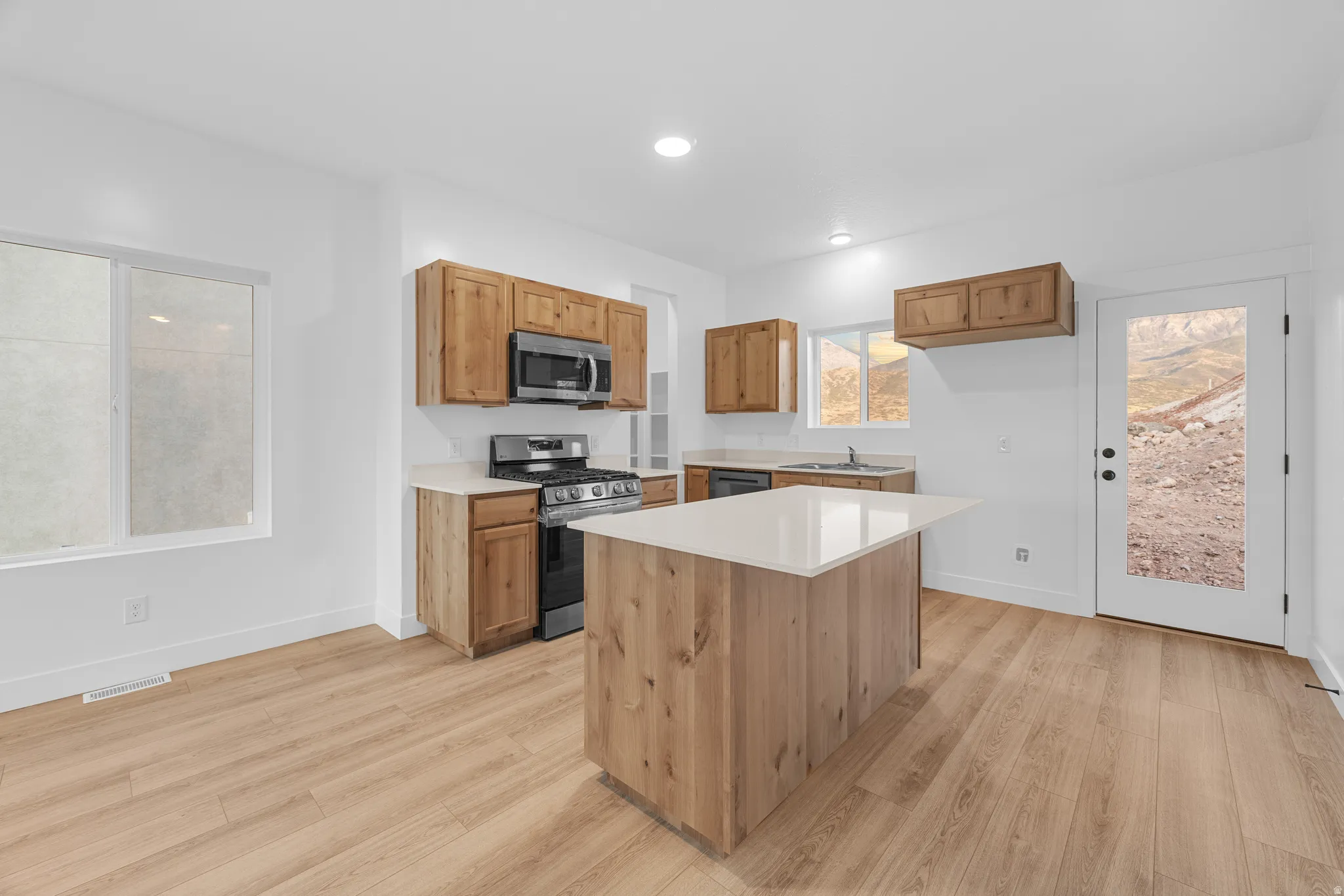 Kitchen featuring wood-finish cabinetry, stainless steel appliances, a center island with a light-toned countertop, and wood-finish flooring