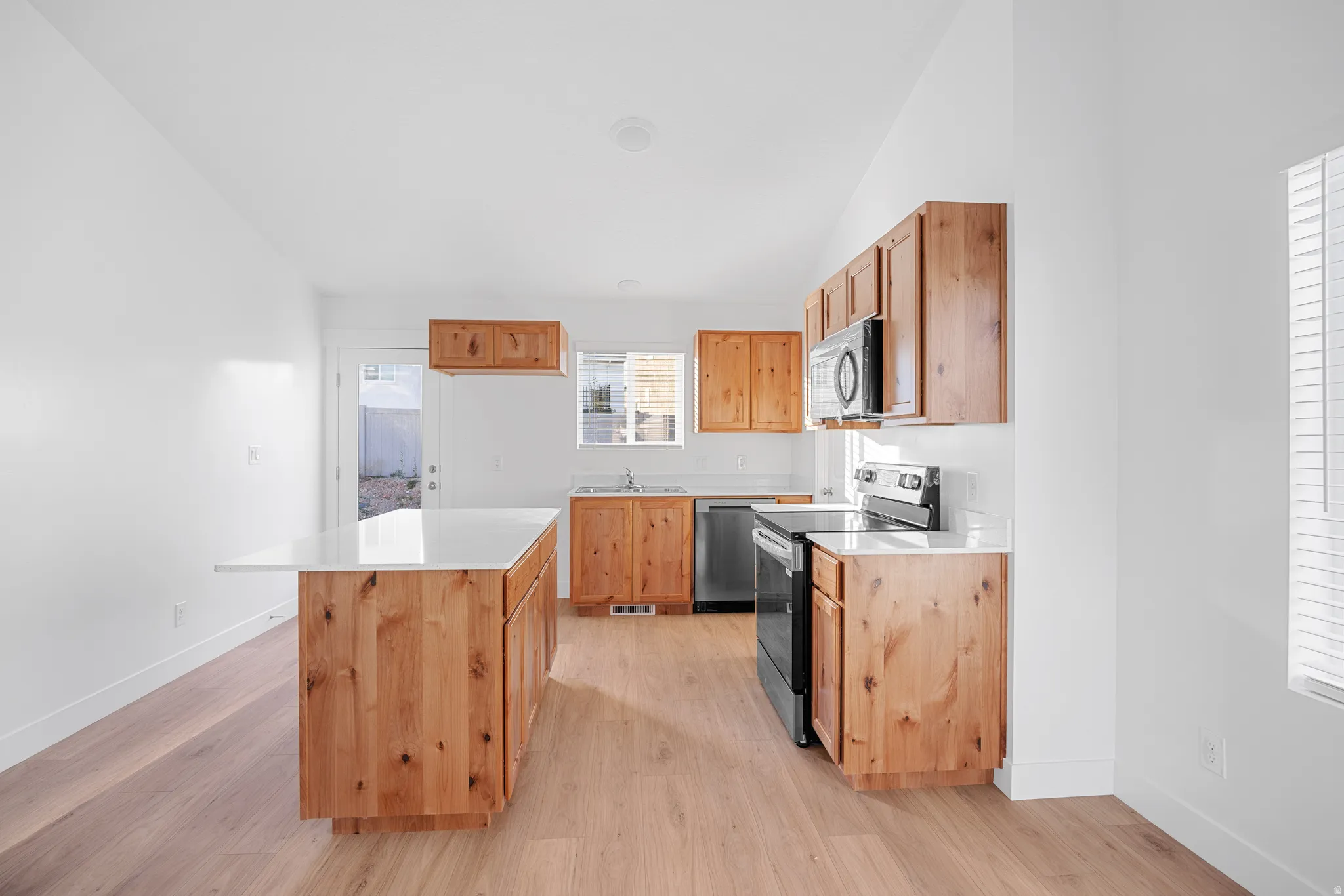 Kitchen featuring wood-finish cabinetry, a central island with white countertop, stainless steel and black appliances, and wood-finish flooring