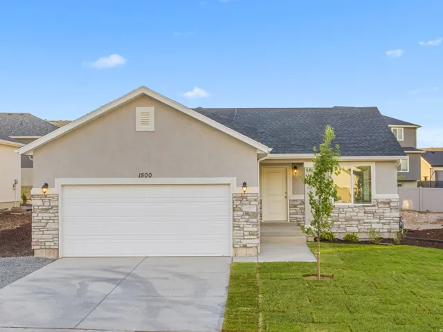 Stucco exterior with stone veneer accents, attached two-car garage, concrete driveway, and a front lawn with young trees