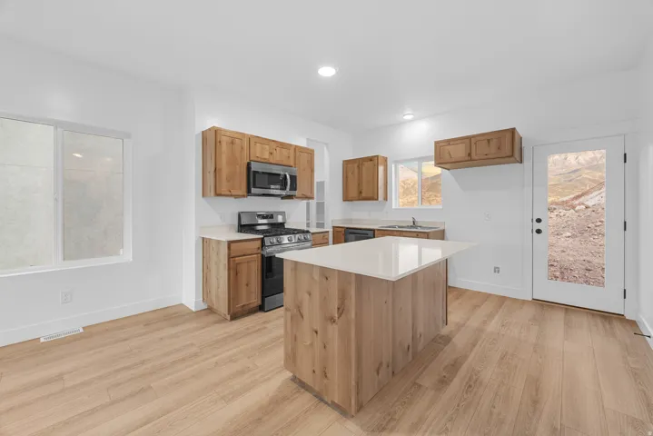 Kitchen featuring wood-finish cabinetry, stainless steel appliances, a center island with a light-toned countertop, and wood-finish flooring