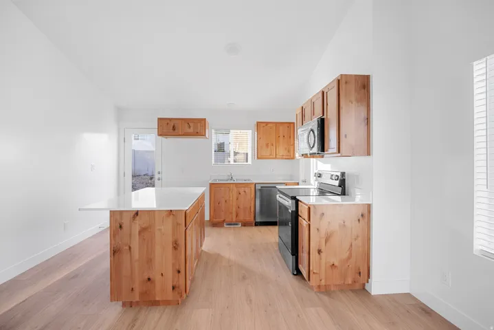 Kitchen featuring wood-finish cabinetry, a central island with white countertop, stainless steel and black appliances, and wood-finish flooring