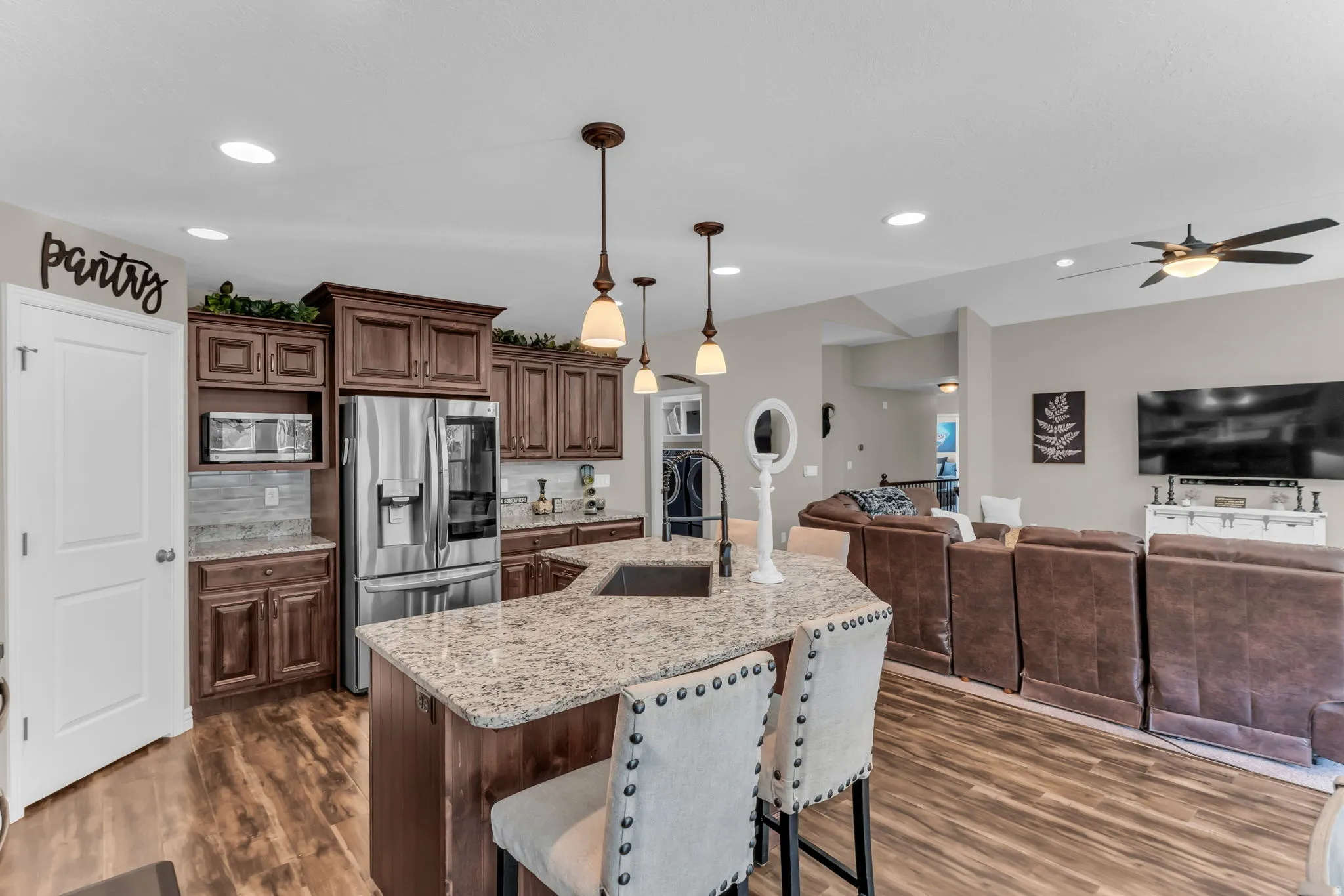 Wood-finish flooring throughout, kitchen with dark wood cabinetry, stainless steel appliances, and a stone-finish countertop island with integrated sink