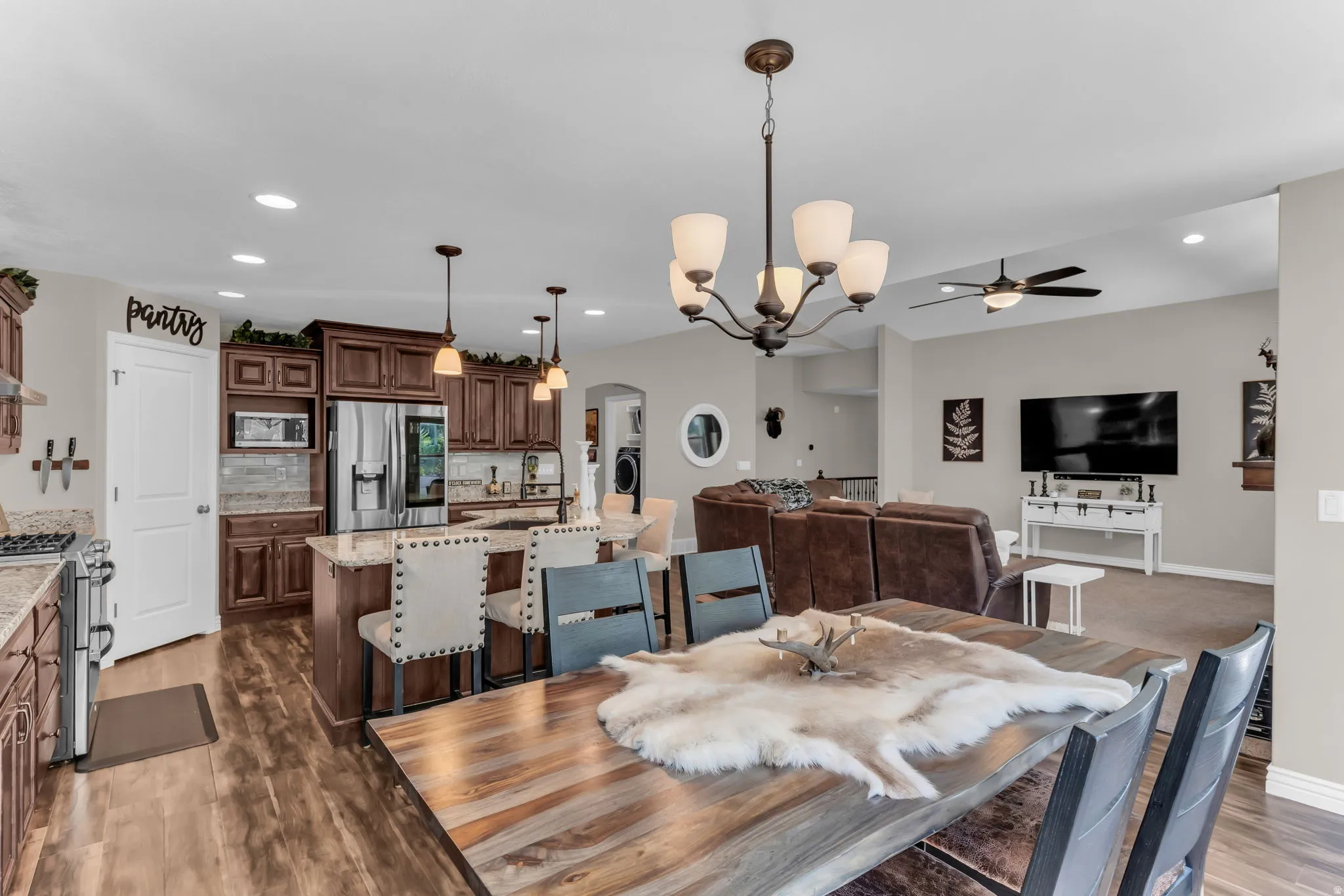 Open-concept living area featuring wood-finish flooring, a kitchen island with seating, dark wood cabinetry, stainless steel appliances, and recessed lighting