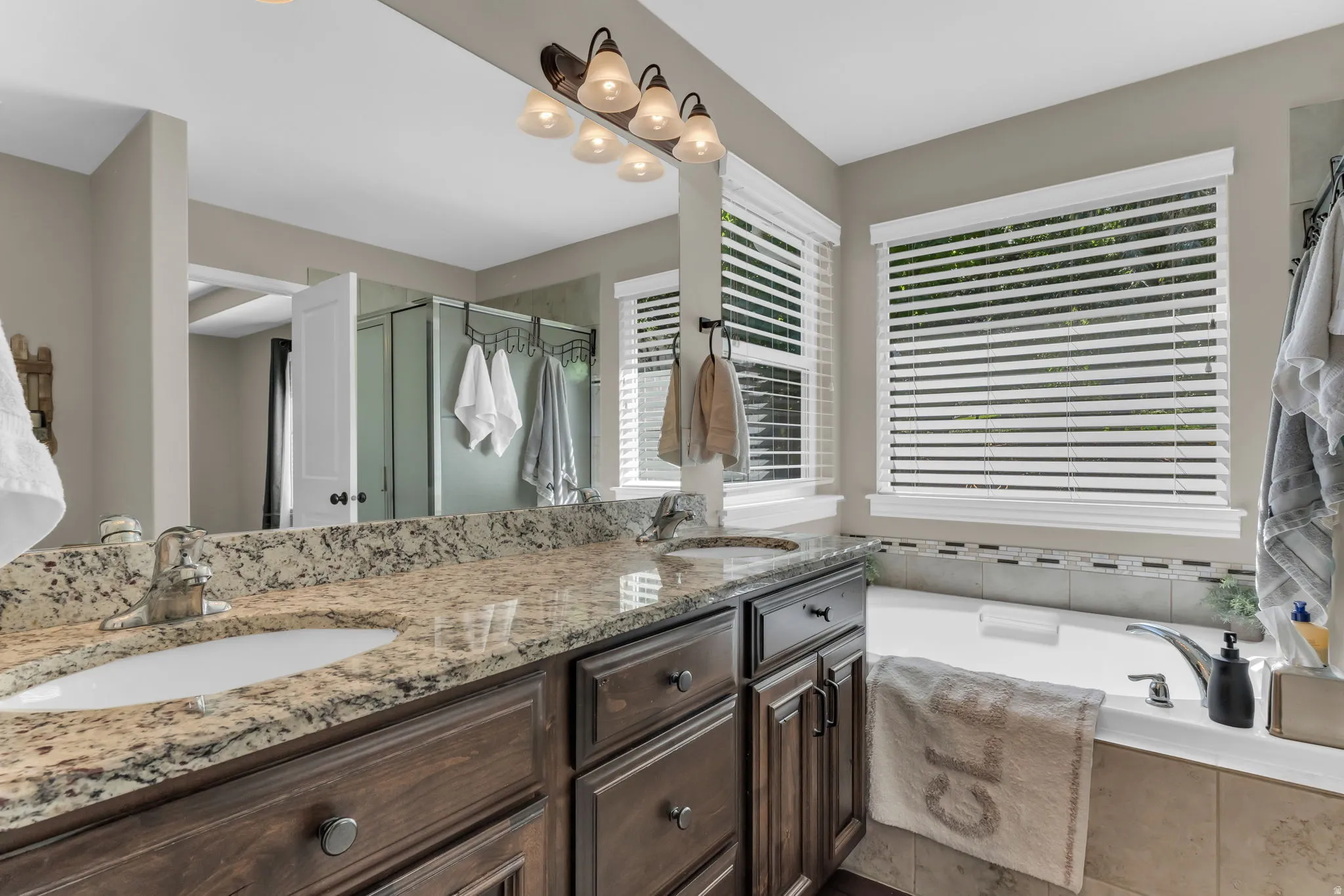 Double vanity with granite countertop, wood cabinetry, built-in soaking tub, and tiled surround