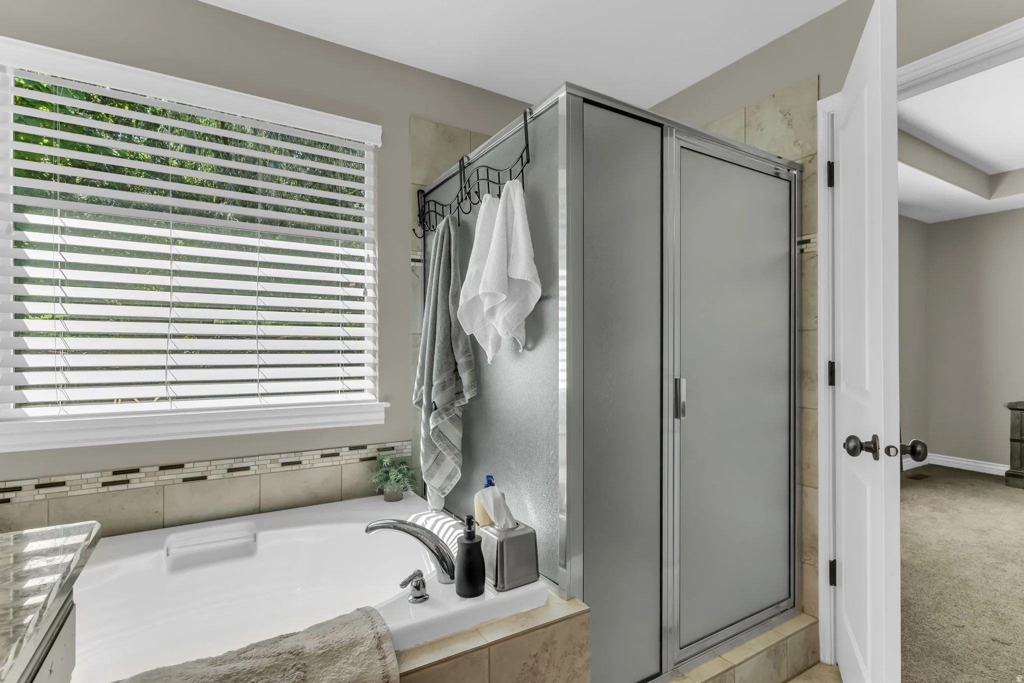Soaking tub with tile surround, glass-enclosed shower, and window with privacy blinds