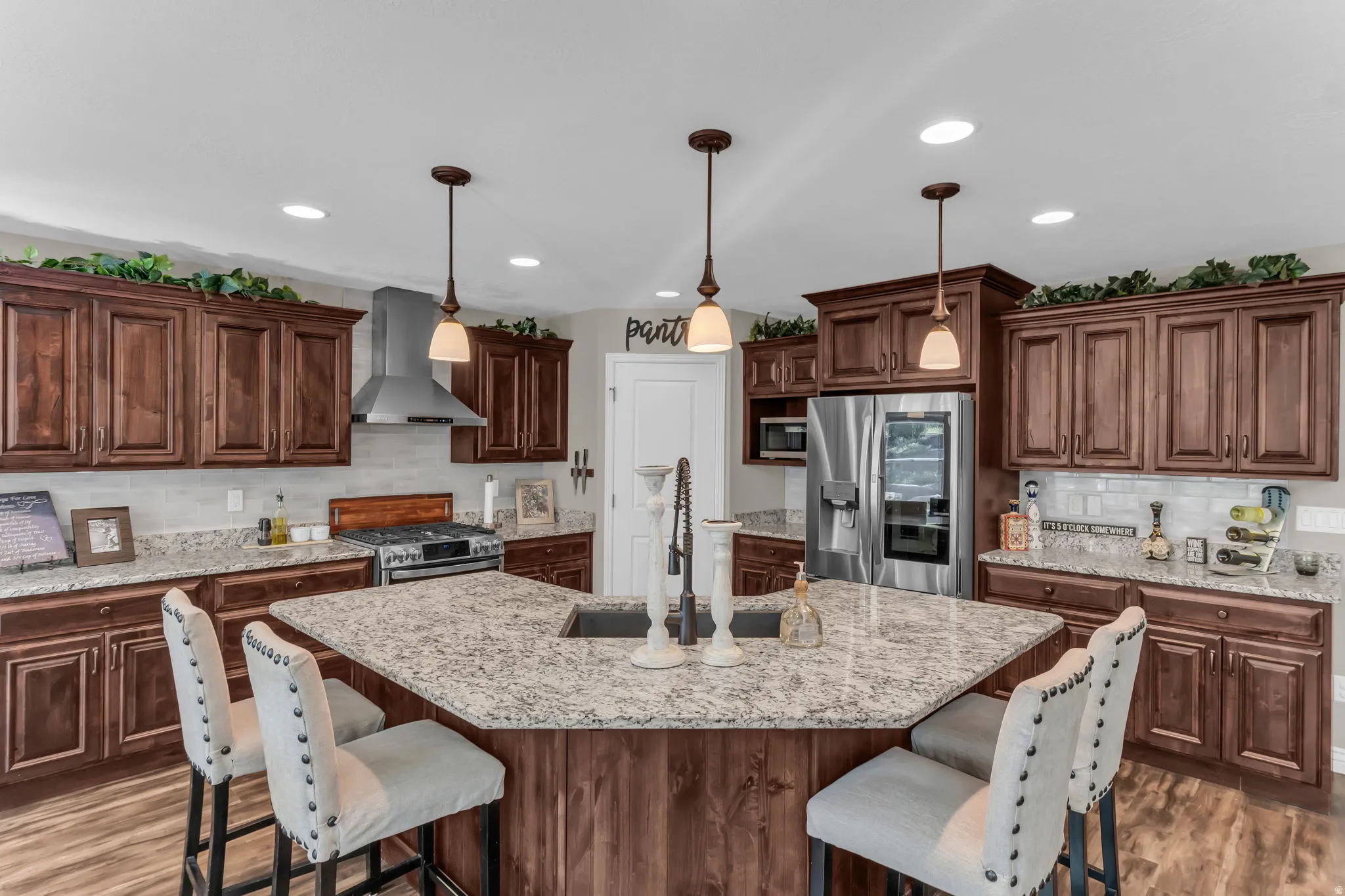 Kitchen featuring dark wood-finish cabinetry, light speckled countertops, a stainless steel range hood, stainless steel refrigerator, and wood-finish flooring