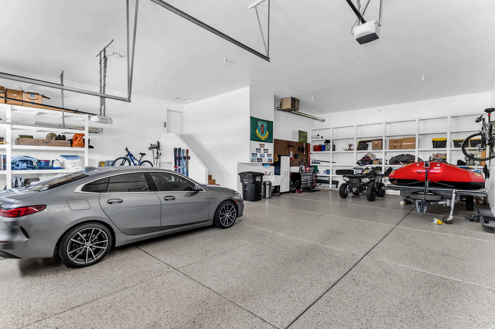 Spacious garage with an epoxy-coated floor, built-in shelving, white painted walls, and a staircase leading to an interior level