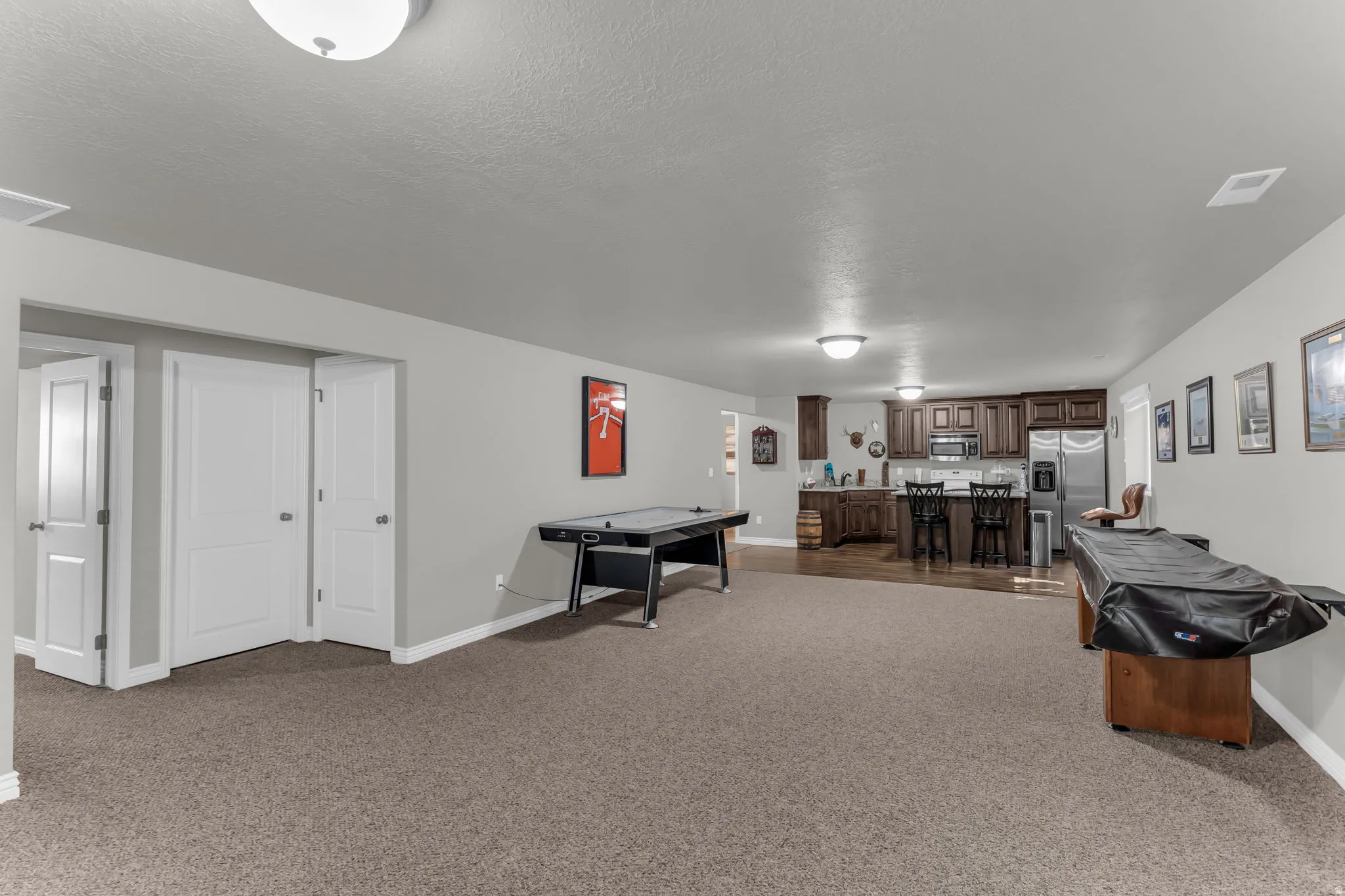 Expansive recreation space featuring recessed lighting, carpeted flooring, and a built-in wet bar with wood cabinetry and stainless steel appliances