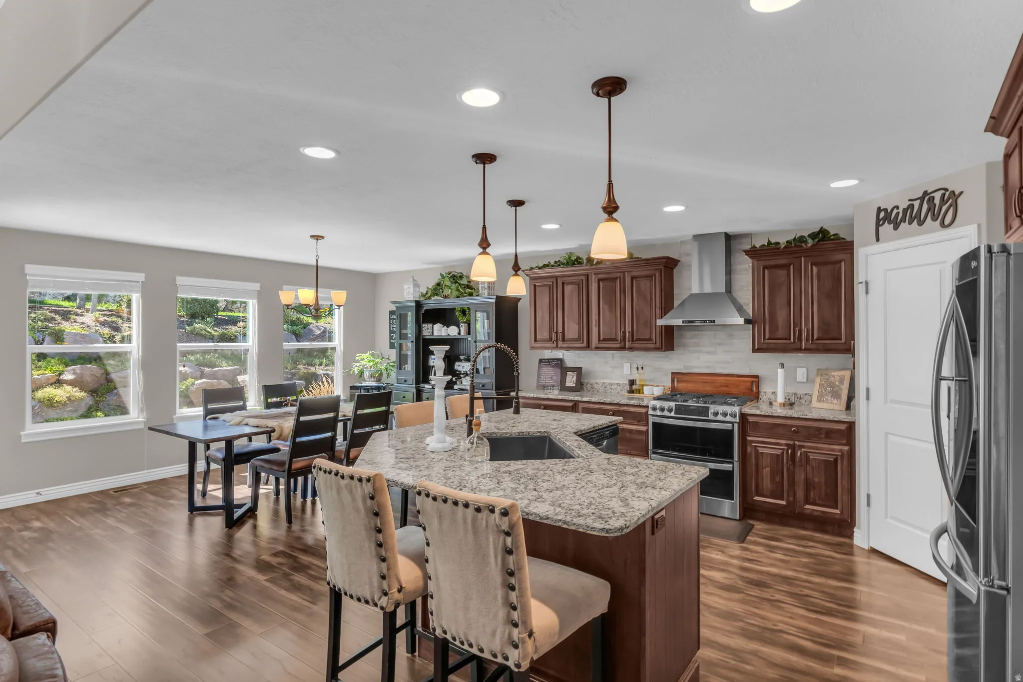 Kitchen featuring wood-finish flooring, dark wood cabinetry, stainless steel appliances, and a central island with a sink and pendant lighting