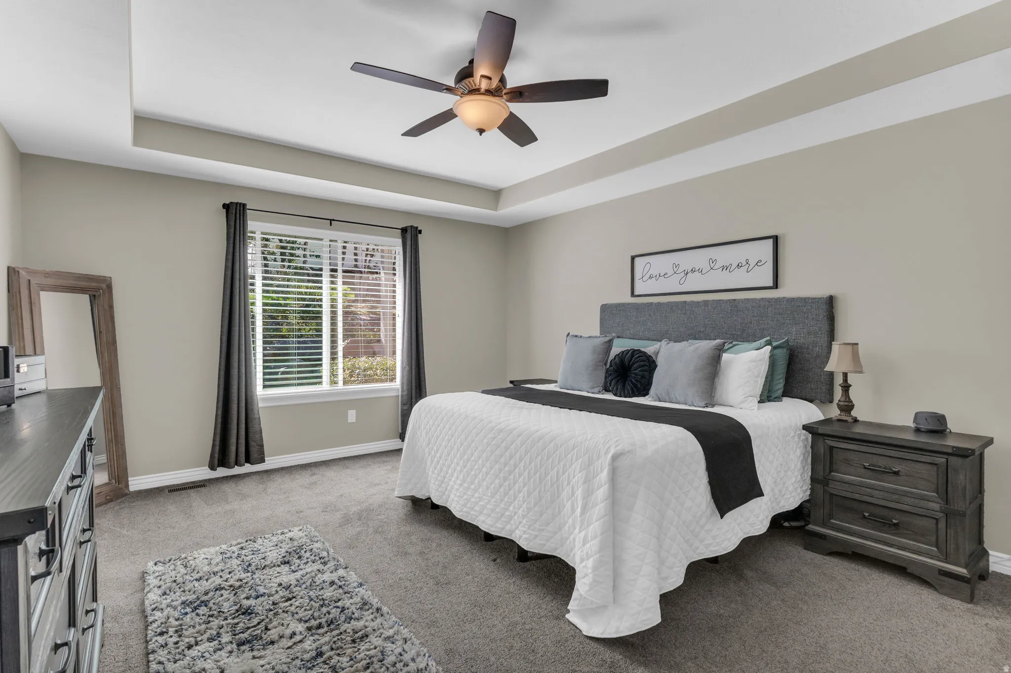 Tray ceiling with a ceiling fan, recessed window, and gray carpeting