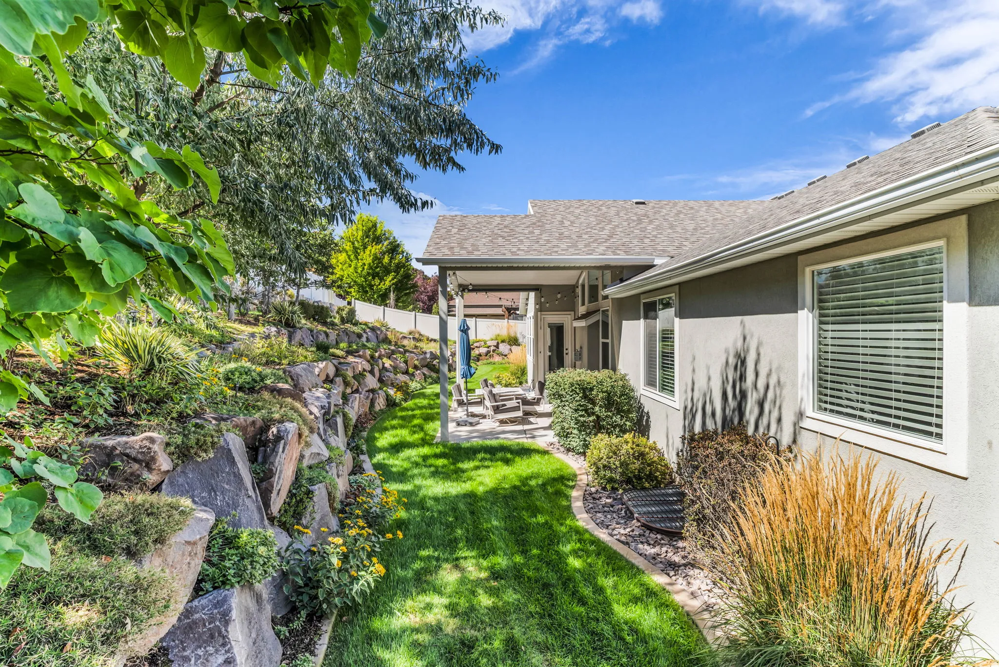 Landscaped exterior featuring a rock retaining wall, mature plantings, and a covered patio with stone steps
