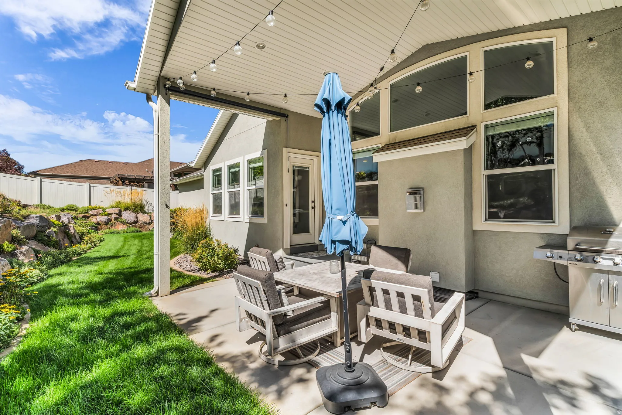 Covered concrete patio with string lighting, expansive lawn, and rock landscaping