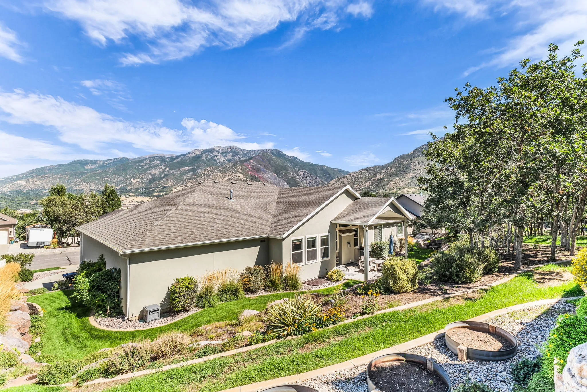 Stucco exterior with a pitched shingle roof, surrounded by mature trees and landscaping