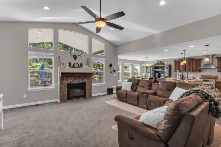 Vaulted ceilings with recessed lighting, stone-clad fireplace, and an open-concept design to the kitchen featuring wood cabinetry and stainless steel appliances