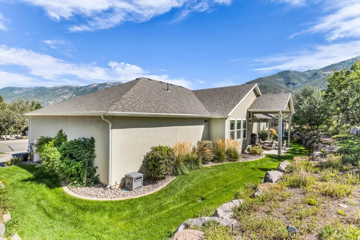 Stucco exterior with a pitched shingle roof, featuring a covered patio, terraced landscaping, and a manicured lawn