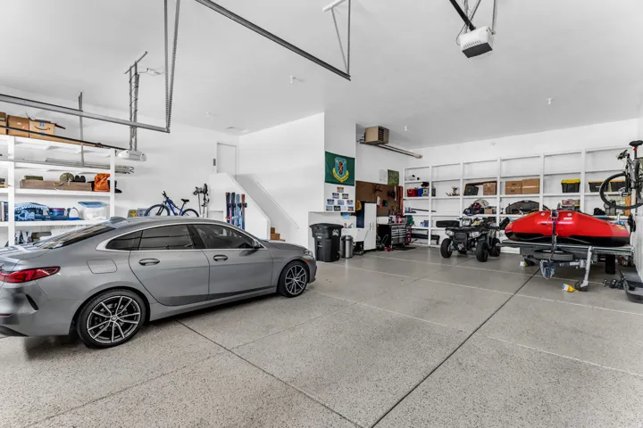 Spacious garage with an epoxy-coated floor, built-in shelving, white painted walls, and a staircase leading to an interior level