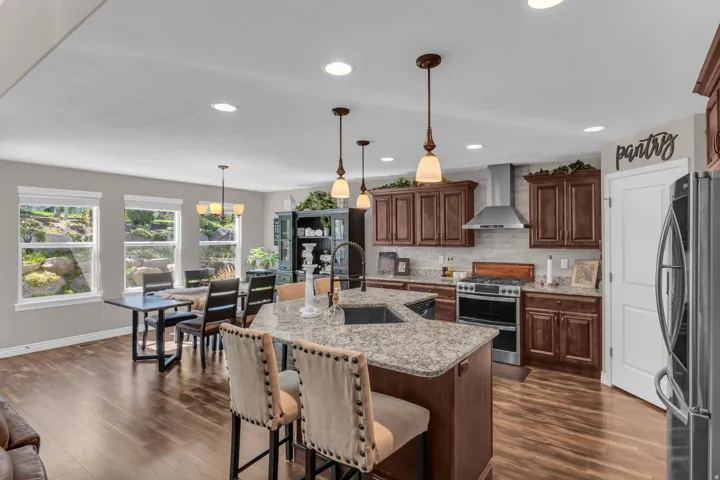 Kitchen featuring wood-finish flooring, dark wood cabinetry, stainless steel appliances, and a central island with a sink and pendant lighting