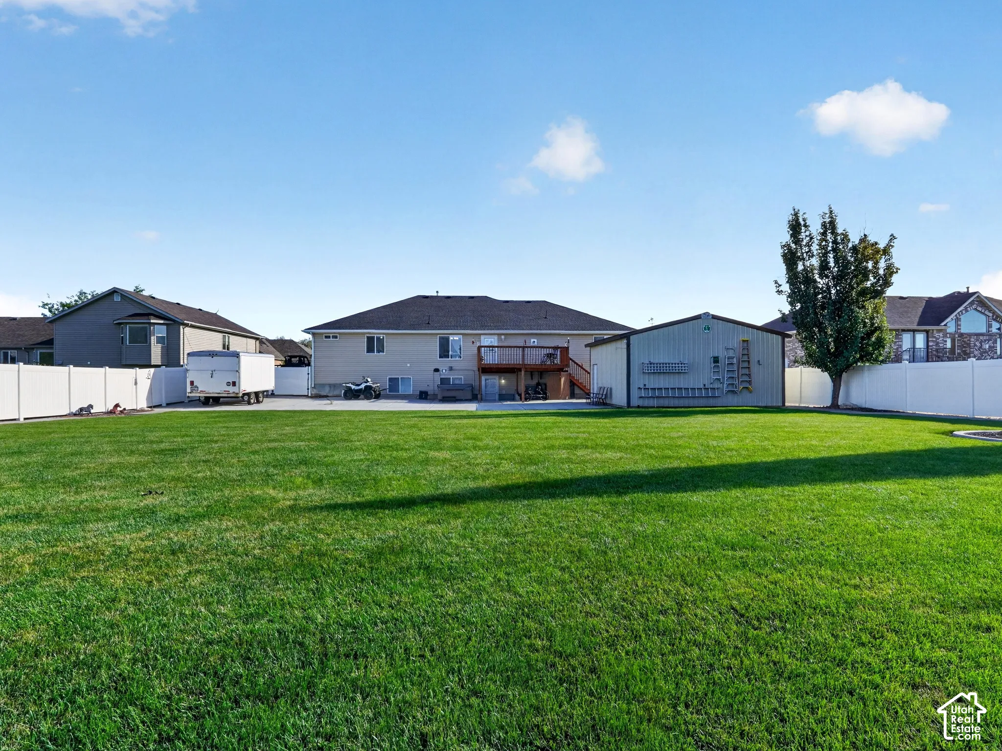 Expansive lawn with a white privacy fence, detached outbuilding, and mature tree