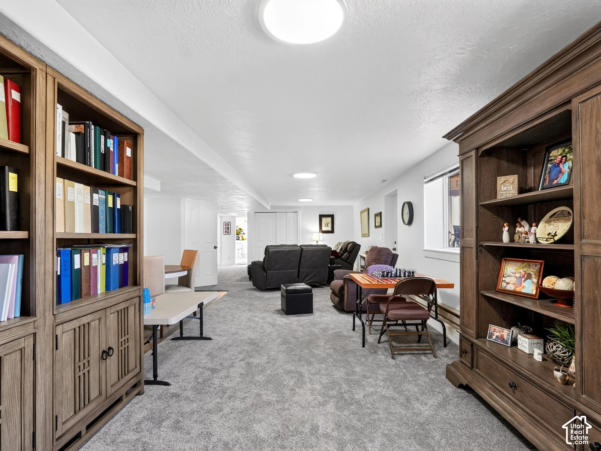 Spacious room with light gray carpeting, recessed ceiling lighting, and built-in wood-finish shelving