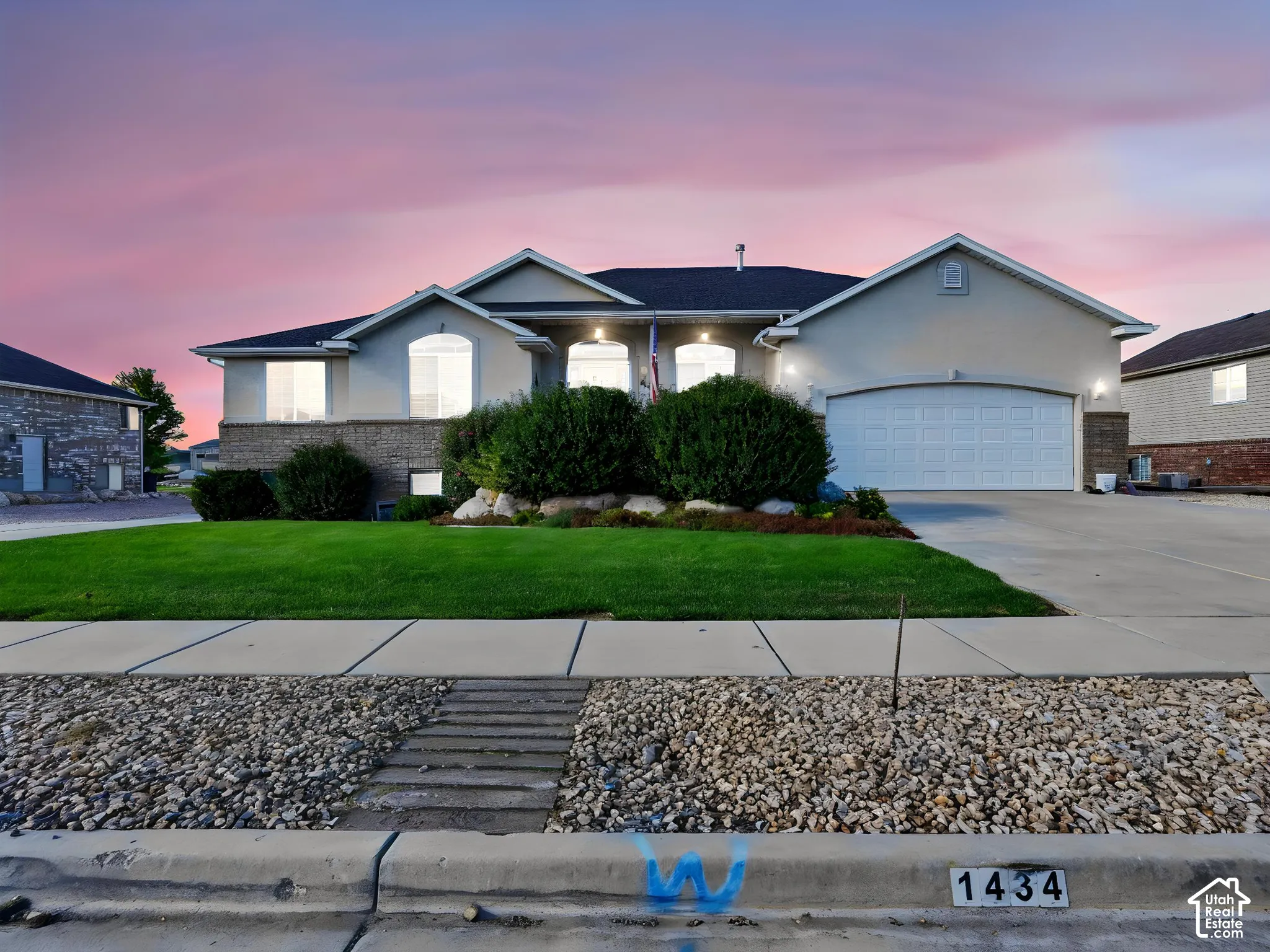 Stucco exterior with stone accent, arched windows, attached two-car garage, concrete driveway, and established front landscaping