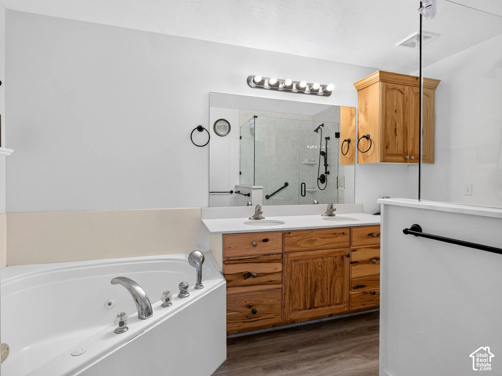 Dual-sink vanity with wood cabinetry, corner soaking tub, and a glass-enclosed shower with black fixtures