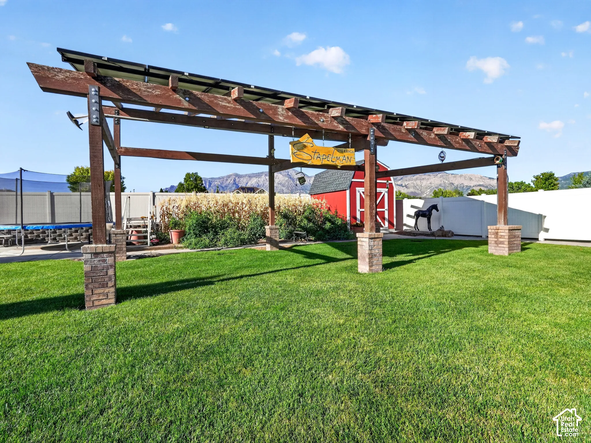 Wood pergola with stone-clad bases, expansive lawn area, red-painted barn structure, and mountain backdrop