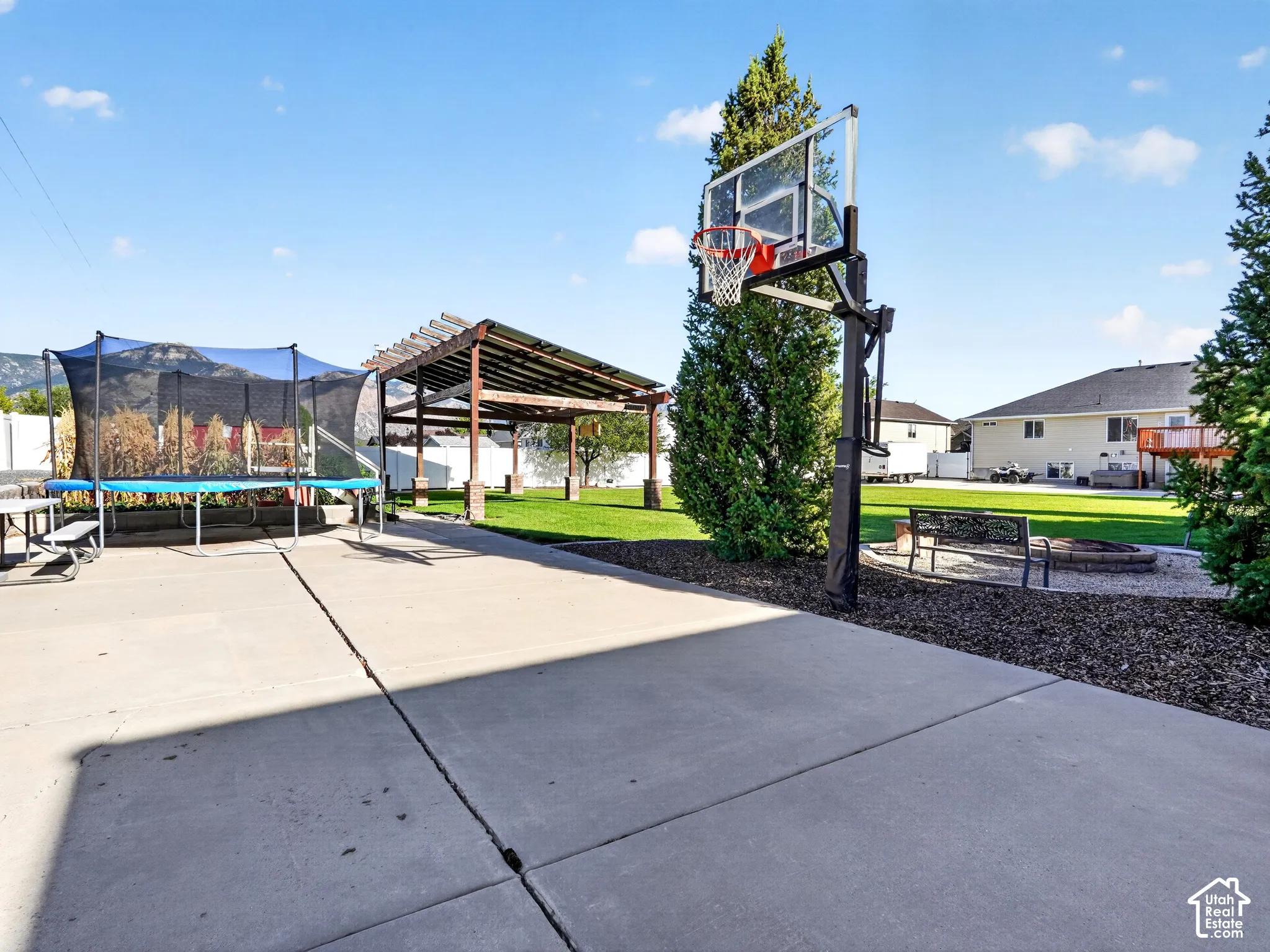 Concrete patio, mature landscaping, pergola, basketball hoop, and a stone-edged fire pit