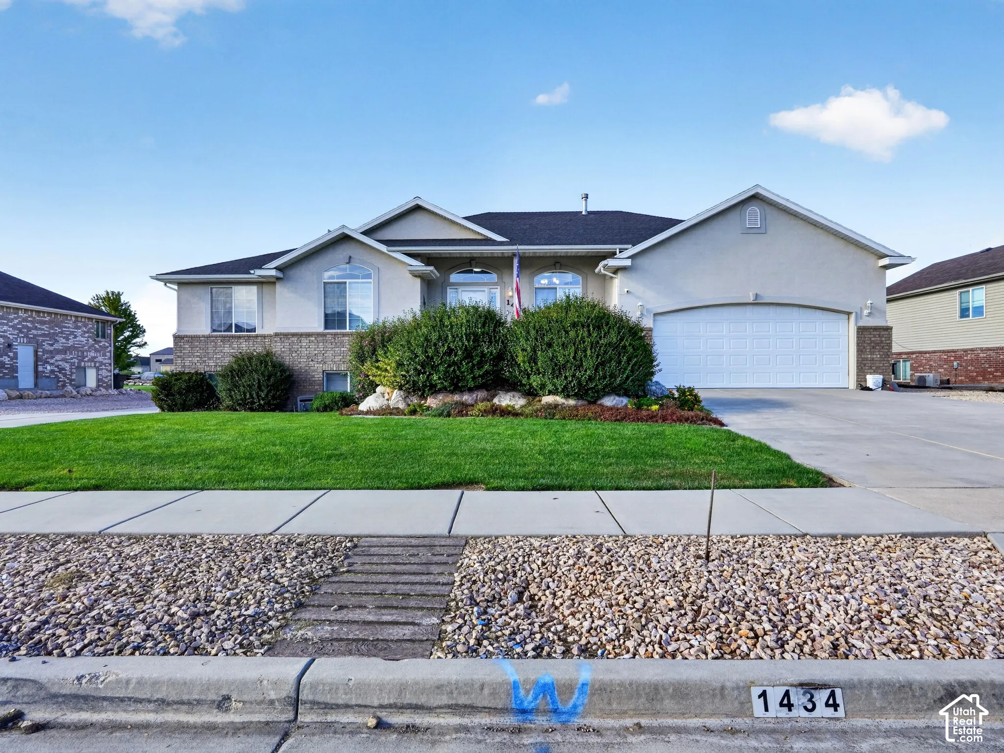 Stucco exterior with brick accent, attached garage, manicured lawn, and established shrubbery