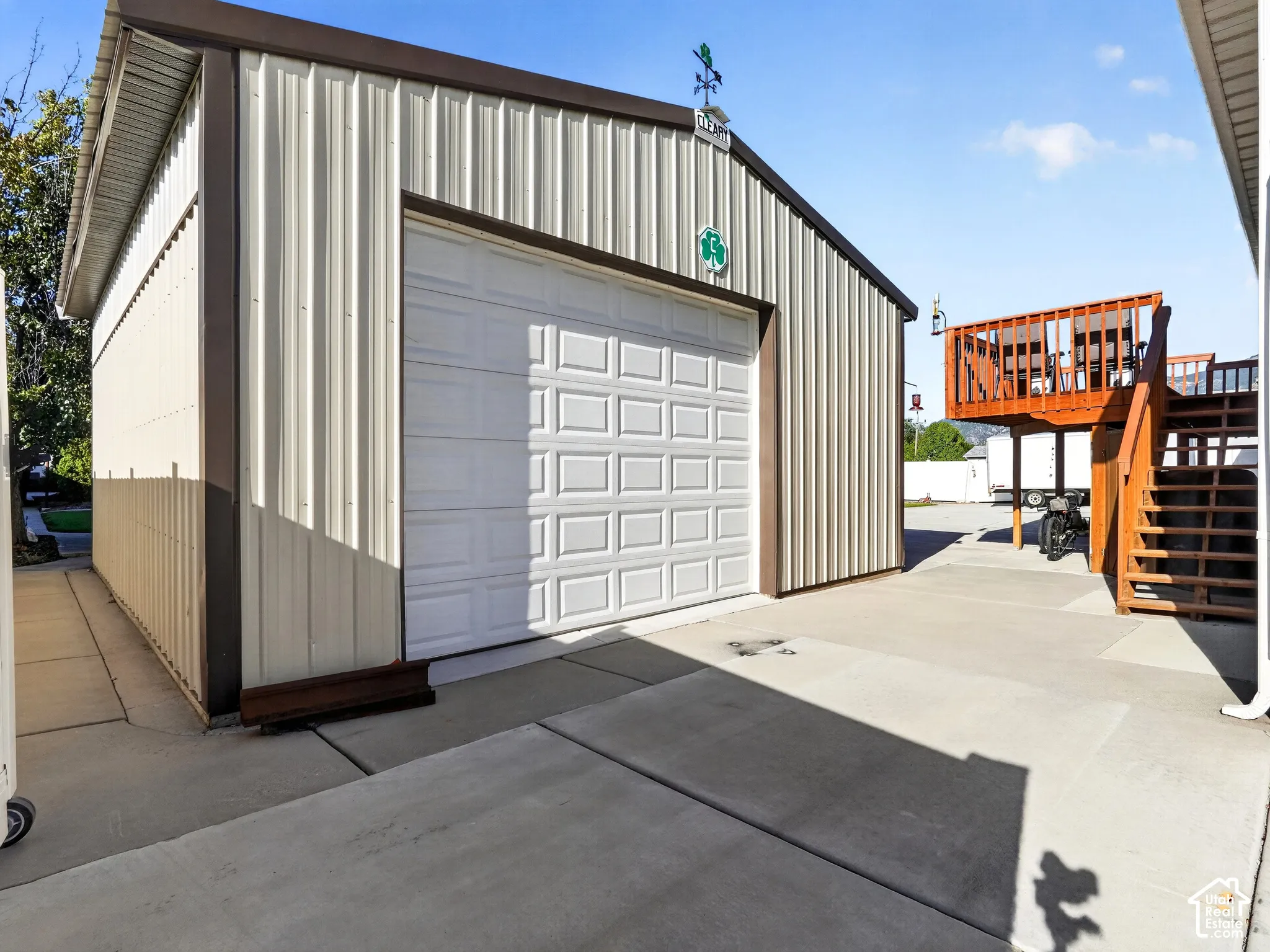 Corrugated metal exterior with a single garage door, concrete drive, and an exterior wood deck with stairs